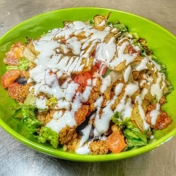 Rico's Taco's taco salad with lettuce, tomatoes, ground meat, and white sauce in a green bowl.