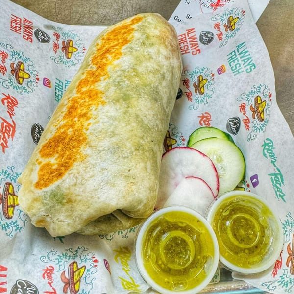 A large Rico's Tacos burrito with two cups of green salsa, cucumber, and radish slices.