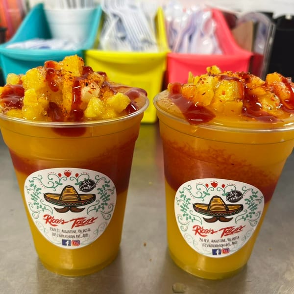 Two Rico's Tacos mango drinks with chili powder and sauce, against a colorful background.