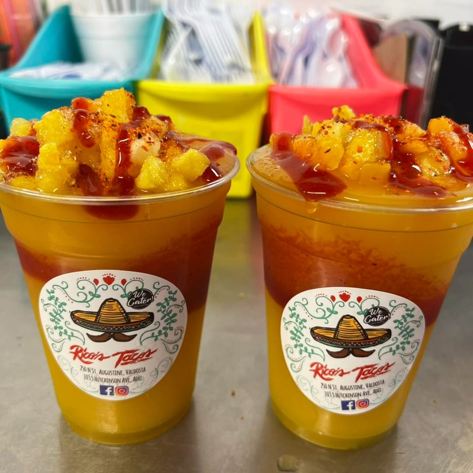 Two Rico's Tacos mango drinks with chili powder and sauce, against a colorful background.