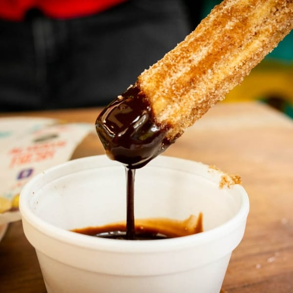 A churro, coated in cinnamon sugar, being dipped into a cup of rich chocolate sauce.