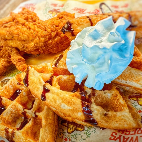 Crispy fried chicken and waffles drizzled with syrup and topped with whipped cream.