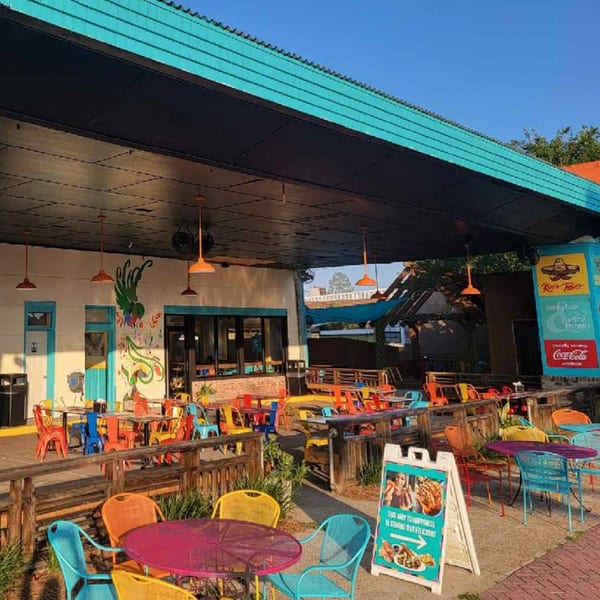 Rico's Tacos vibrant outdoor patio with colorful tables and chairs under a teal awning.