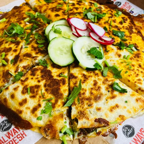 A large, golden-brown quesadilla from Rico's Tacos, cut into wedges, topped with cilantro, cucumber, and radish slices.