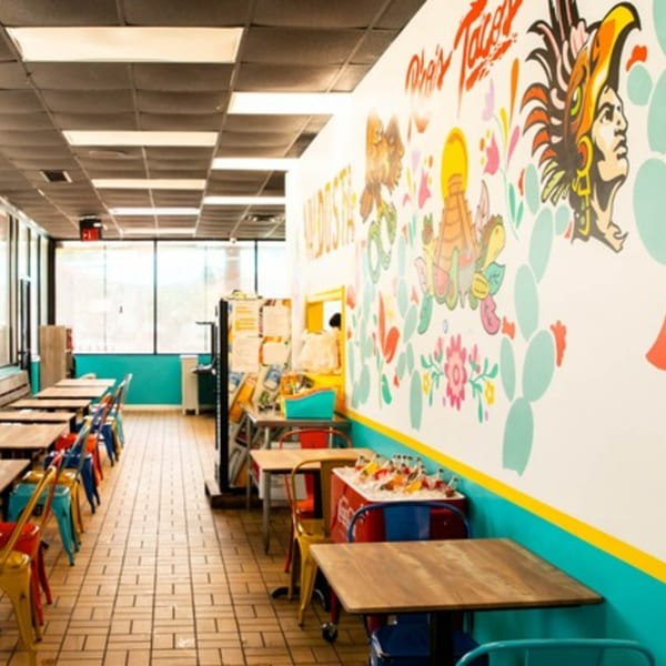 Interior of Rico's Tacos with colorful mural, wooden tables, and bright chairs.