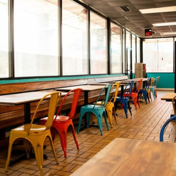 Rico's Tacos dining area with colorful chairs, wooden tables, and large windows.