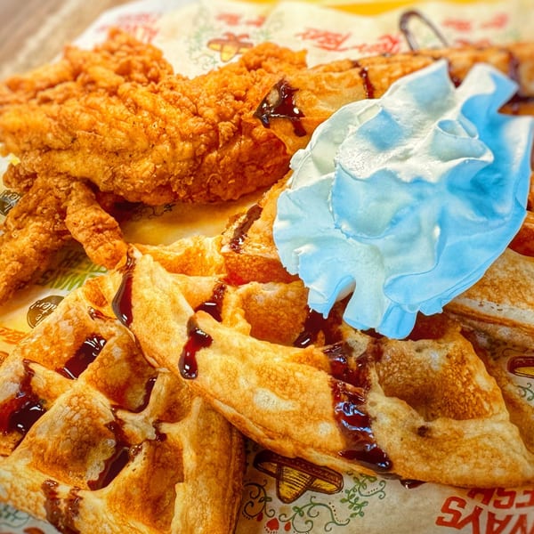 Crispy fried chicken and waffles drizzled with syrup and topped with whipped cream.