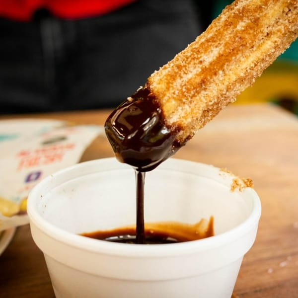 A churro, coated in cinnamon sugar, being dipped into a cup of rich chocolate sauce.