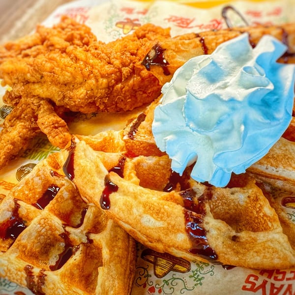 Crispy fried chicken tenders and waffles drizzled with syrup and topped with whipped cream.